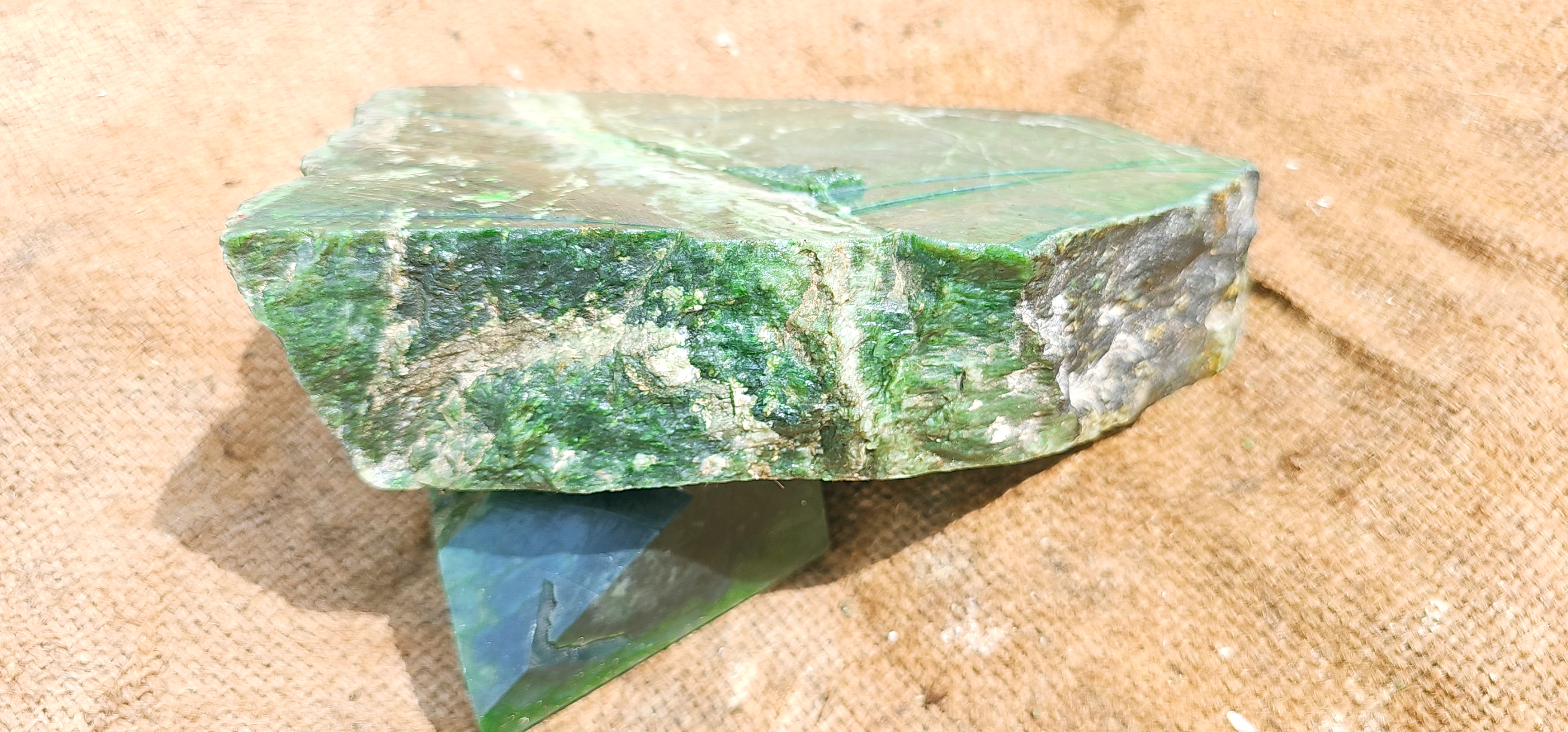 This Natural Green Jade Rough Stone features a beautiful range of natural green tones, from softer translucent green areas to deeper green sections. The stone displays distinctive natural veining, mineral patterns, and subtle variations throughout its sur